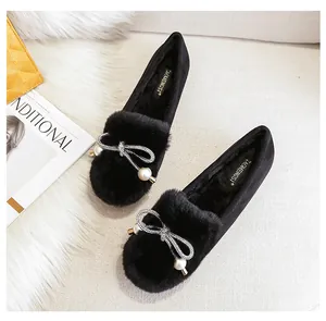 Detail of plush black loafers with rhinestone bow and pearl accents on fur background