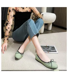 Close-up of light green ballet flats with black bow detail on a white textured rug