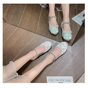 Detail of satin ballet flats featuring rhinestone strap and bow on polished wood floor