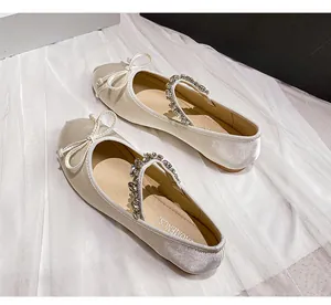 Close-up of ivory satin Mary Jane ballet flats with rhinestone strap and bow detail