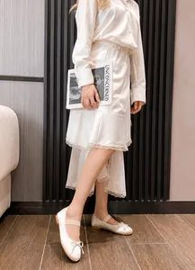 Detailed view of white ballet flats with bow and elastic straps worn by model