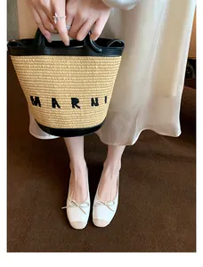 Dettaglio delle ballerine bicolore con fiocco indossate con borsa di paglia sullo sfondo