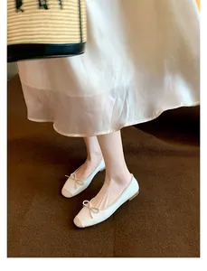 Dettaglio di ballerine bianche a punta quadrata con fiocco su tappeto scuro