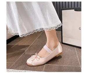 Close-up of pink satin ballet flats with a bow detail and elastic strap on a model