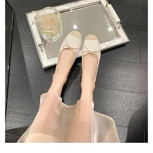 Vista dall'alto di ballerine francesi con punta beige e fiocco su pavimento in legno scuro