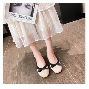 Detail von eleganten beige-schwarzen Ballerinas mit Schleife an einem Model auf Holz