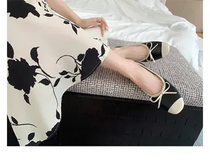 Dettaglio di eleganti ballerine bicolore con fiocco indossate su uno sgabello