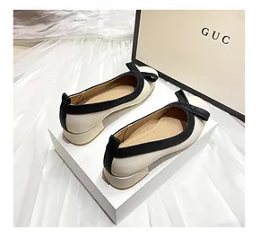 Elegante cremefarbene Pumps mit schwarzem Kontrastrand und Schleife auf weißem Dekor