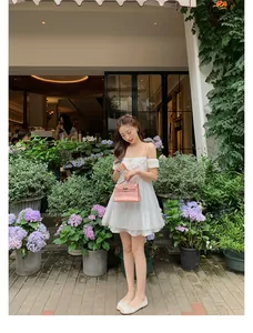 Dettaglio di una borsa in pelle rosa tenuta da una modella in un abito estivo bianco