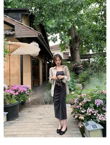 Set chic con abito grigio aderente e cardigan beige trasparente in un giardino