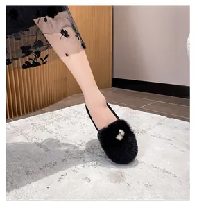 Detail of black plush loafers with metal buckle and floral dress on a grey carpet