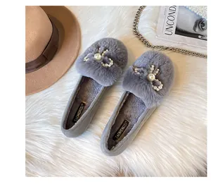 Detail of grey plush slip-on shoe featuring a pearl and rhinestone bow on a soft rug