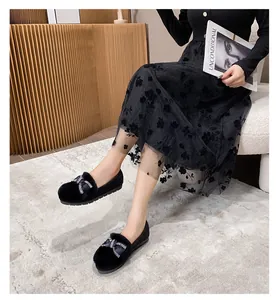 Dettaglio di mocassini neri in peluche con fiocco di strass indossati con gonna a fiori
