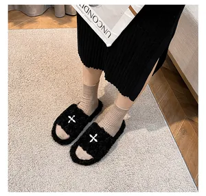 Close-up of black faux fur slippers with white X design on a textured carpet