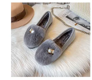 Detail of grey fur loafers with plush lining and gold buckle on a stylish white rug