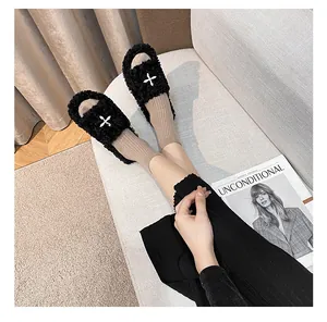 Close-up of black plush slides with white cross embroidery and soft faux fur texture