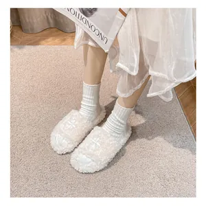 First-person macro view of cream plush slippers with crisscross design on soft rug