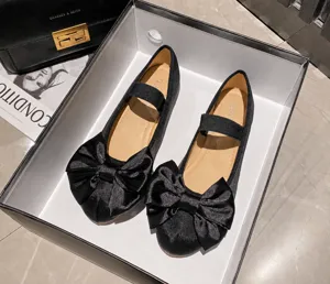 Détail de ballerines Mary Jane en satin noir avec nœud et talon souple dans leur boîte