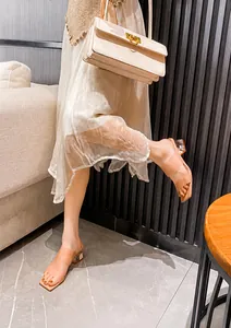 Detail von Damen-Sandalen in Beige mit transparentem Kristallabsatz zu einem weißen Kleid
