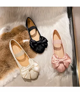 Gros plan sur les ballerines en satin beige, noir et rose avec un grand nœud décoratif