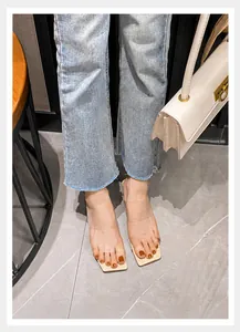 Draufsicht auf eckige transparente PVC-Sandalen mit drei Riemen auf Marmorboden