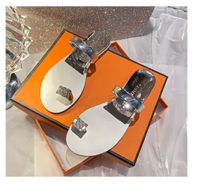 Close-up of silver rhinestone toe-ring sandals with glossy finish on orange box