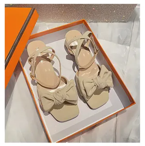 Detalle de sandalias beige de punta cuadrada con lazo grande y cierre de hebilla en caja de regalo