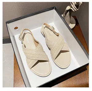 Detailaufnahme der geflochtenen Kreuzriemen und Metallschnalle an flachen beigen Sandalen