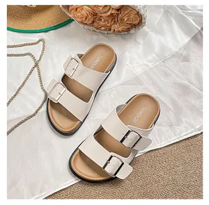 Flat beige double-strap sandals with silver buckles on white silk and summer props