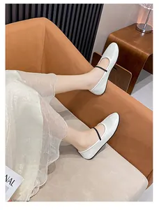 Gros plan de ballerines Mary Jane blanches avec fine bride noire sur un sofa