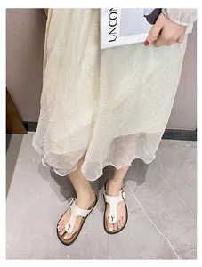 Close-up of off-white toe-thong sandals with gold buckle on a model with a pleated skirt