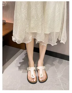 On-foot view of beige flat T-strap sandals with gold buckle and cork-style footbed