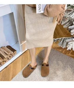 Brown fleece mule with leather buckle strap shown in a warm indoor home setting