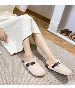 Detail of plush beige mule slippers with leather strap and cork sole on grey carpet