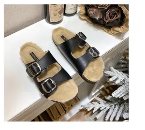 Detailed macro view of black faux leather clogs with warm beige faux fur lining and gold buckles