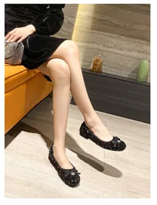 Close-up of black sequined flat shoes with bow and metal buckle on orange sofa