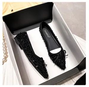 Top-down view of black sequined pointed-toe flats with leather bow in gift packaging