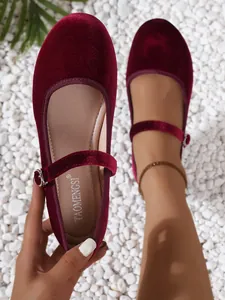 Close-up of burgundy velvet Mary Jane flat shoe with buckle strap on white stones