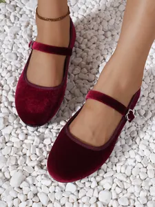 Top view of wine red velvet Mary Jane flats worn on feet over white pebbles background