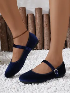 Side view of dark blue velvet Mary Jane flats with metal buckle on white pebbles