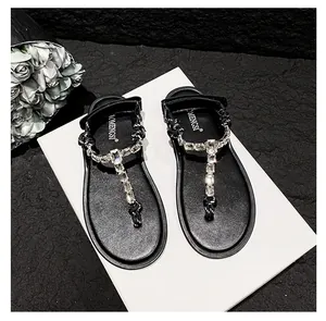 Detail of black flat sandals with sparkling rhinestones and T-strap on a black texture
