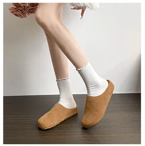Detail of brown suede leather mule slipper worn with white lace socks on wood floor