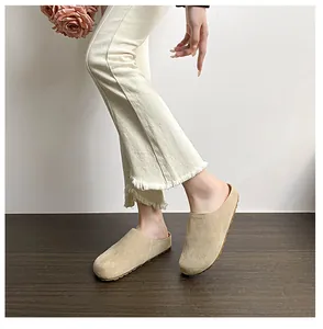 Close-up of khaki suede mule slippers featuring a thick rubber sole on a model foot