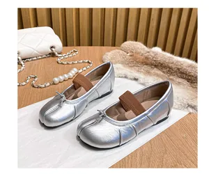 Detail of silver split-toe ballet flats with bow and elastic strap on wooden background