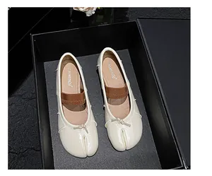 Detail view of cream sheepskin Tabi flats with bow accent and brown elastic strap