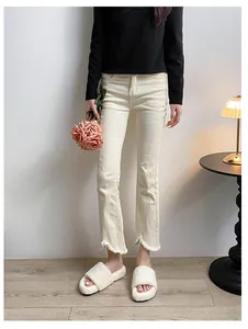 Detail of high-waist cream flared jeans with stylish frayed raw hem and soft cotton denim texture