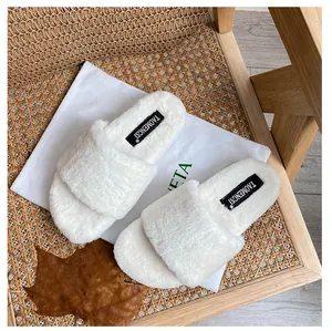 Close-up of white plush fuzzy slippers with brand label on woven rattan chair