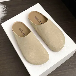 Khaki suede leather mule clog with round toe and flat sole on a textured display box