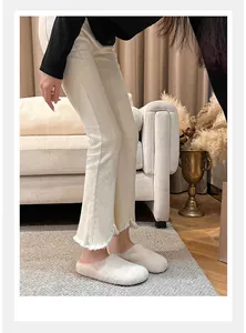 Cozy cream-colored faux fur slippers worn with white flared jeans in a home setting