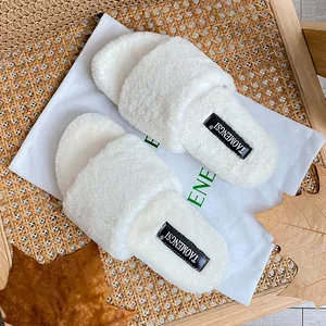 Plush white open-toe faux fur slippers with thick soles and dust bag on rattan chair